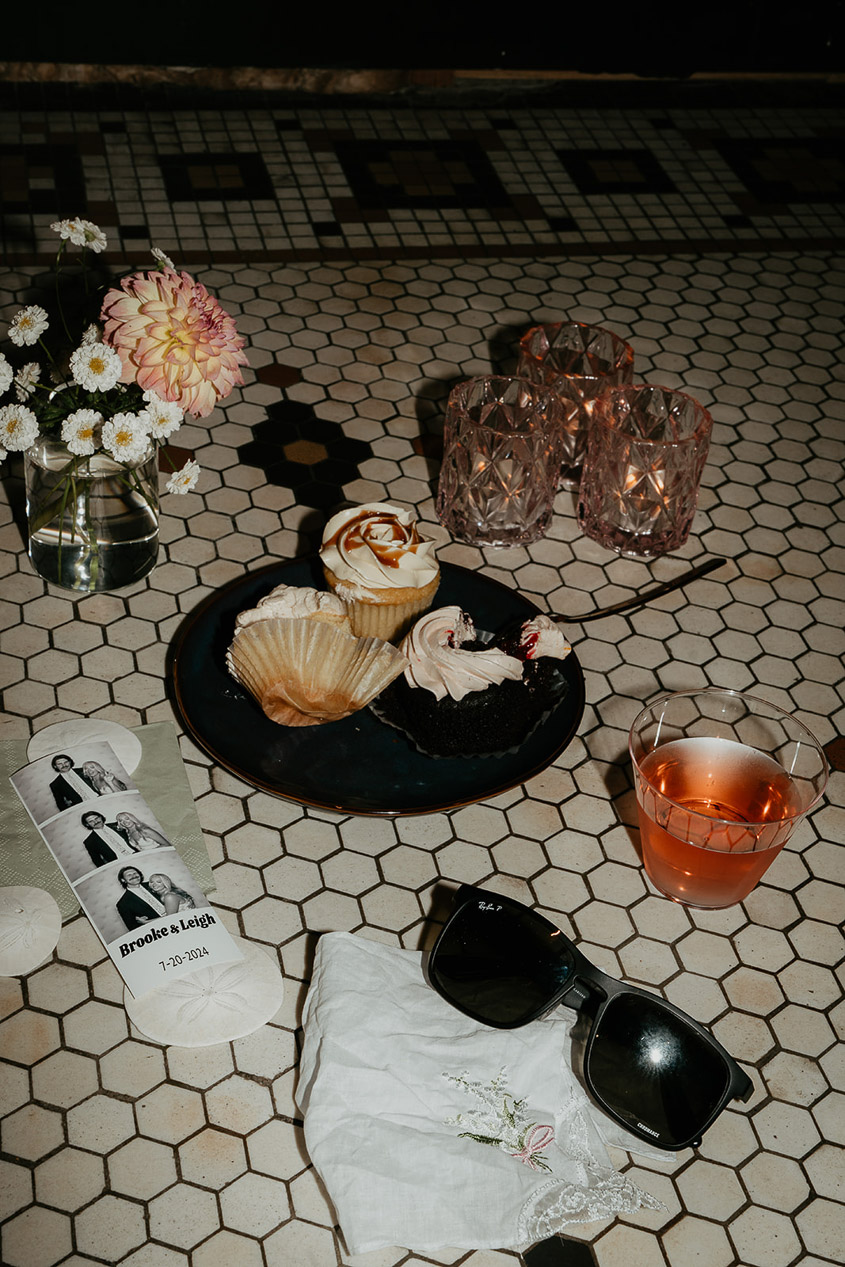 a drink, cupcake, candles, vase of flowers, sunglasses, and Photo Booth photos on a tile floor. 