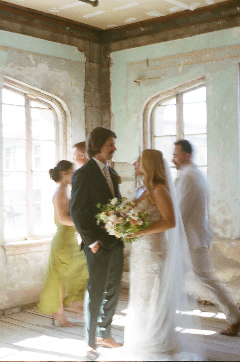 the newlyweds smiling while their wedding party walks behind them.