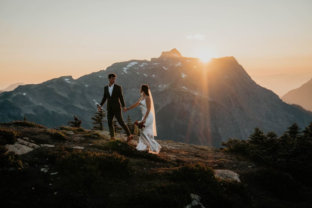 Bride and groom hold hands while walking across a mountain trail while they elope in the North Cascades