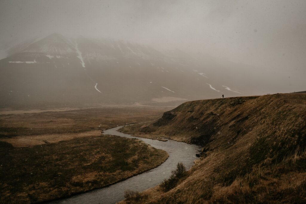 Bride and groom stand on a foggy bluff overlooking a river at their elopement in Iceland 