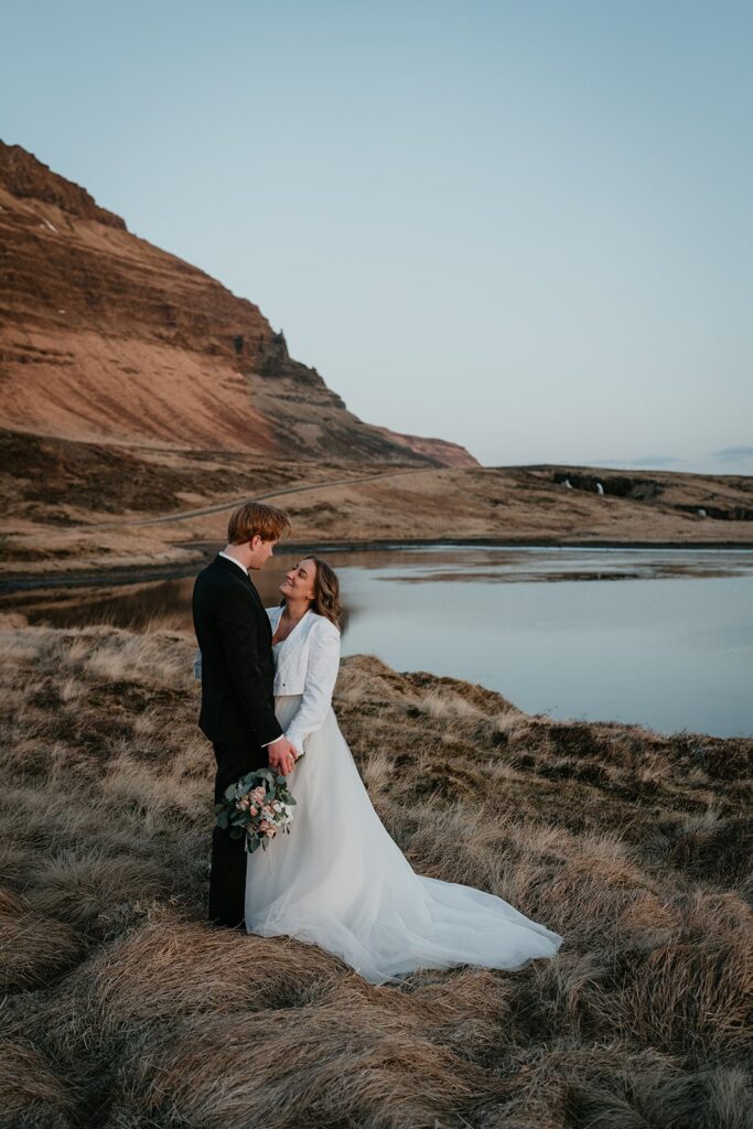 Bride and groom hold hands while standing by a clear pool at their Iceland elopement 