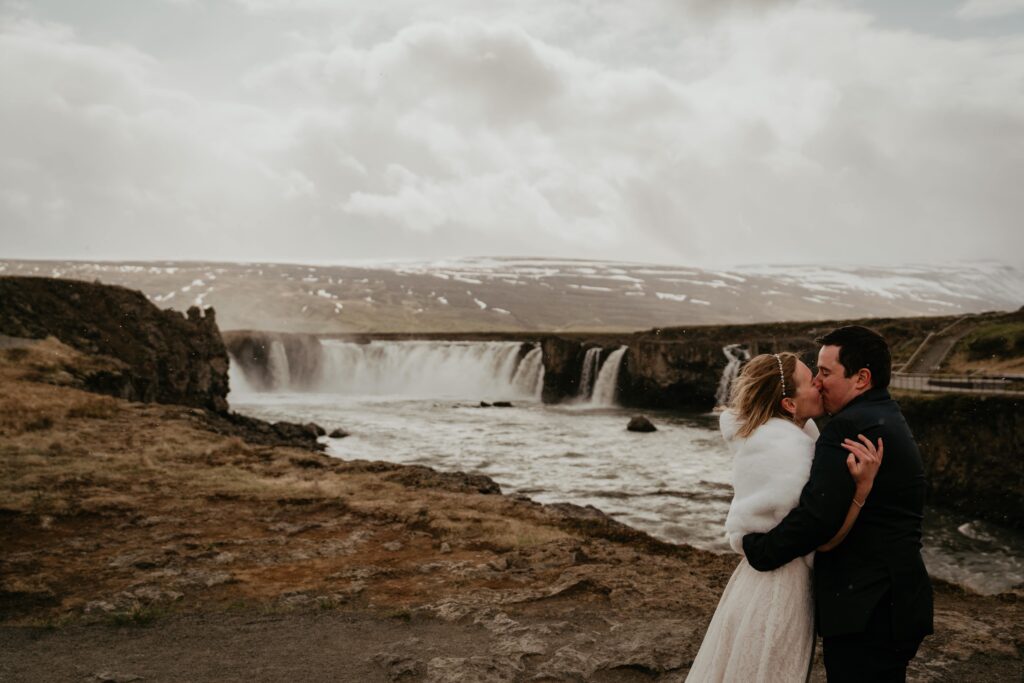 Bride and groom kiss next to a waterfall at their Iceland elopement 