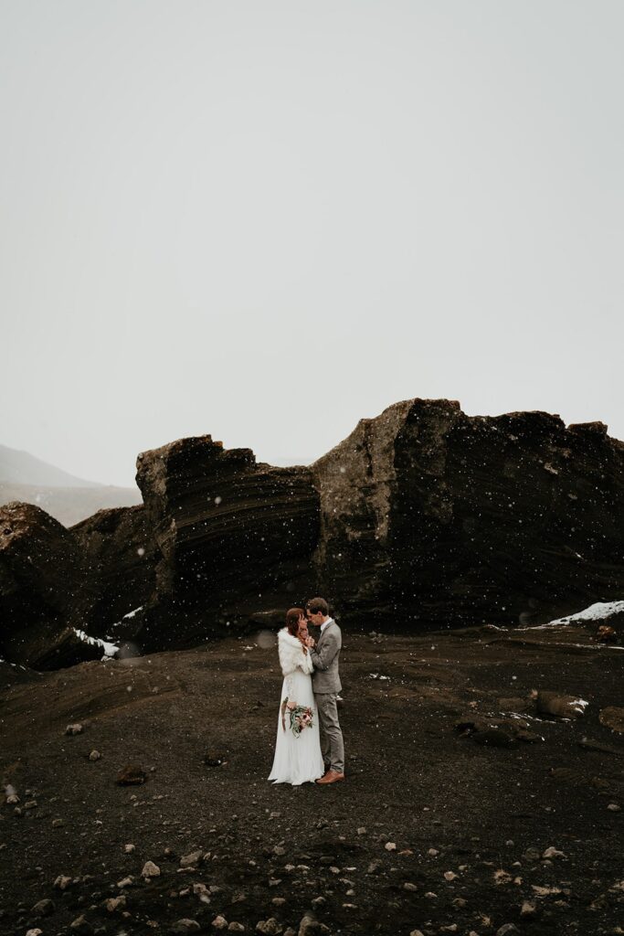 Bride and groom stand on a black sand beach at their Iceland elopement 