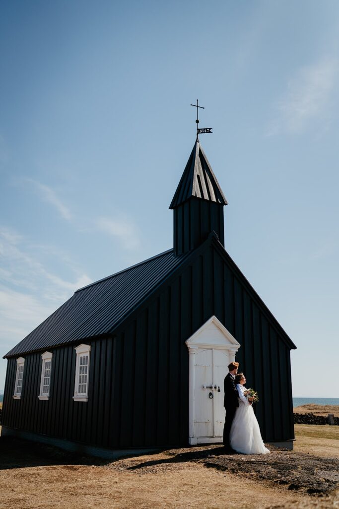 Bride and groom hug while standing in front of The Little Black Church while they elope in Iceland 