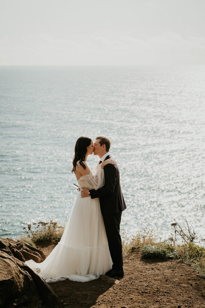 A couple kissing during their Oregon Coast elopement, with the ocean in the background. 