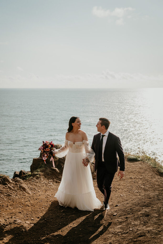 the newlyweds holding hands walking on the Oregon cliffside during their elopement. 