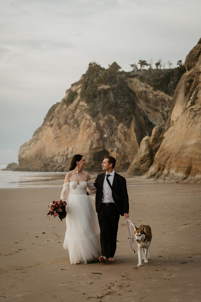 The newlyweds walking along the Oregon coast with their dog during their elopement. 