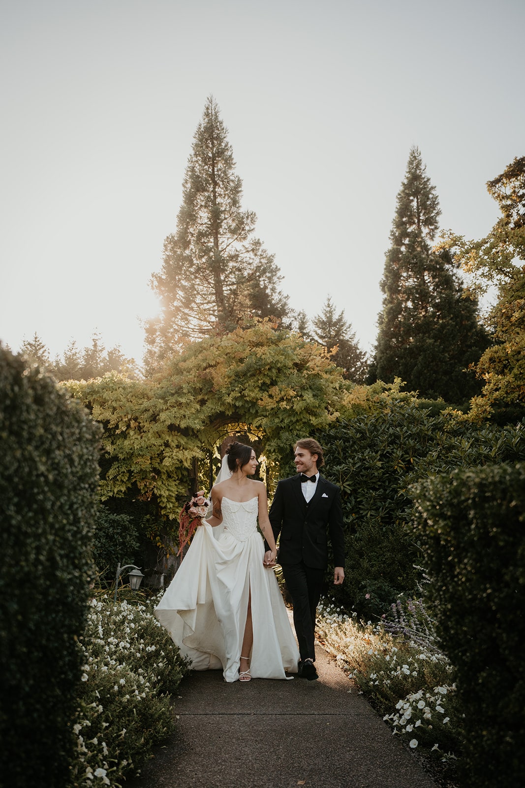 Bride and groom hold hands while walking through the gardens at their wedding venue