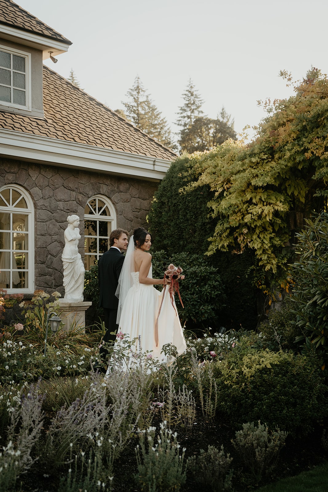 Bride and groom hold hands while walking through the gardens at their wedding venue