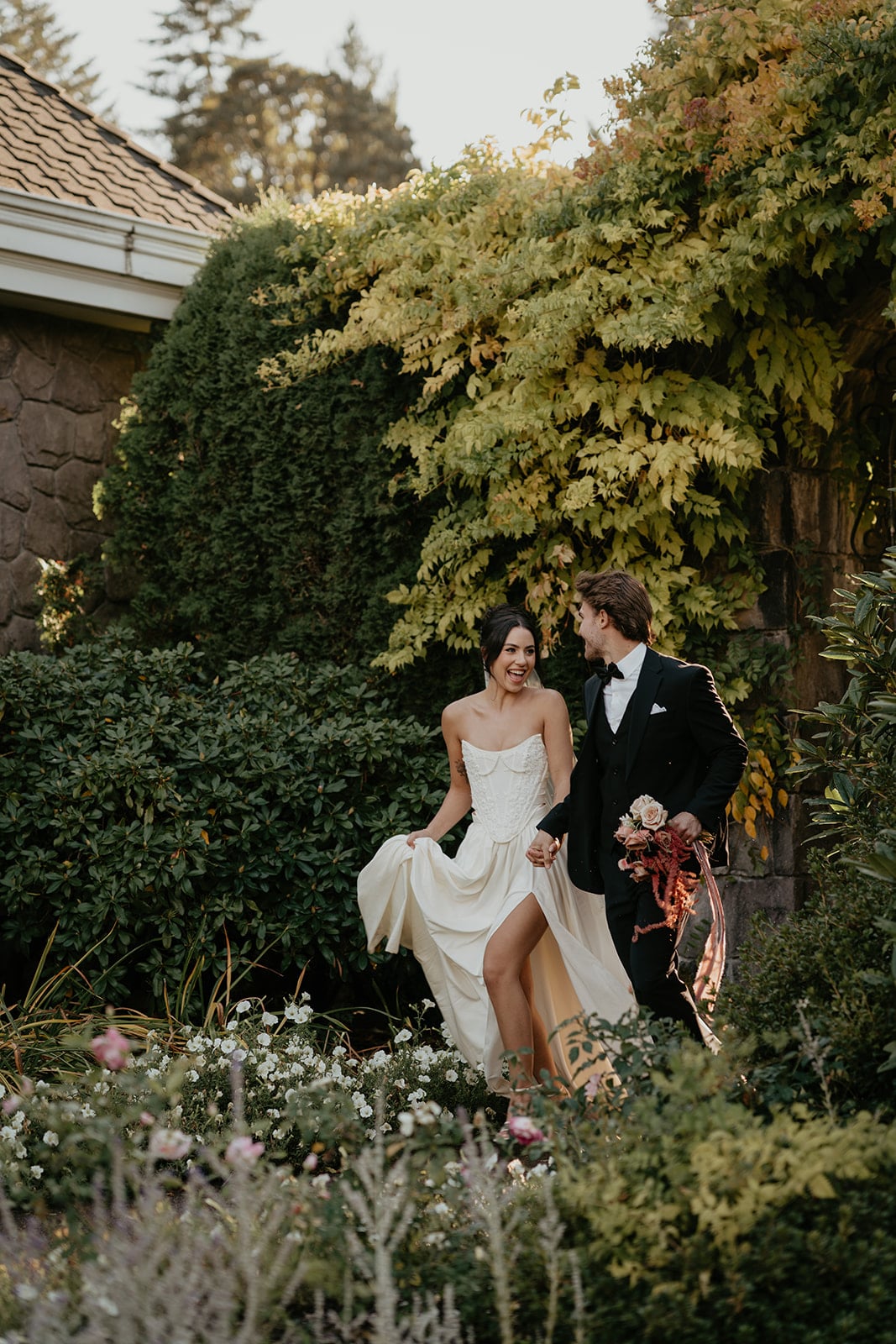 Bride and groom hold hands while running through the gardens at their wedding venue