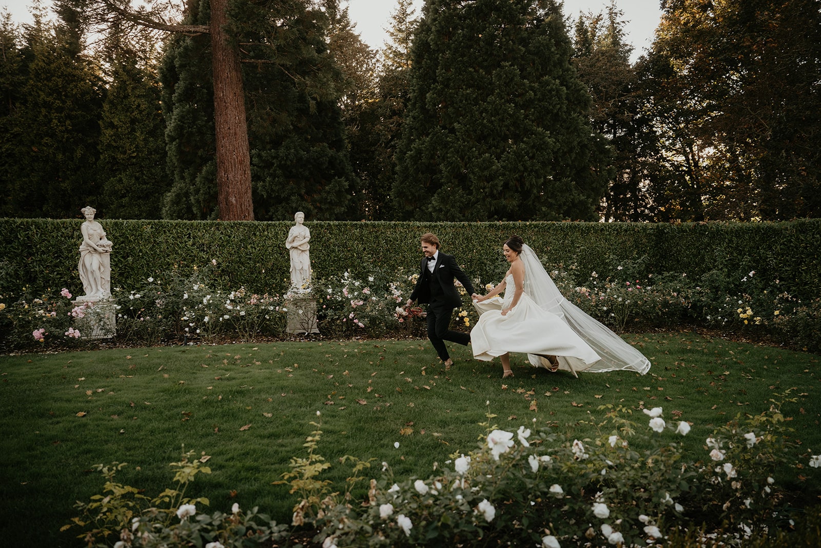 Bride and groom hold hands while running through the gardens at their wedding venue