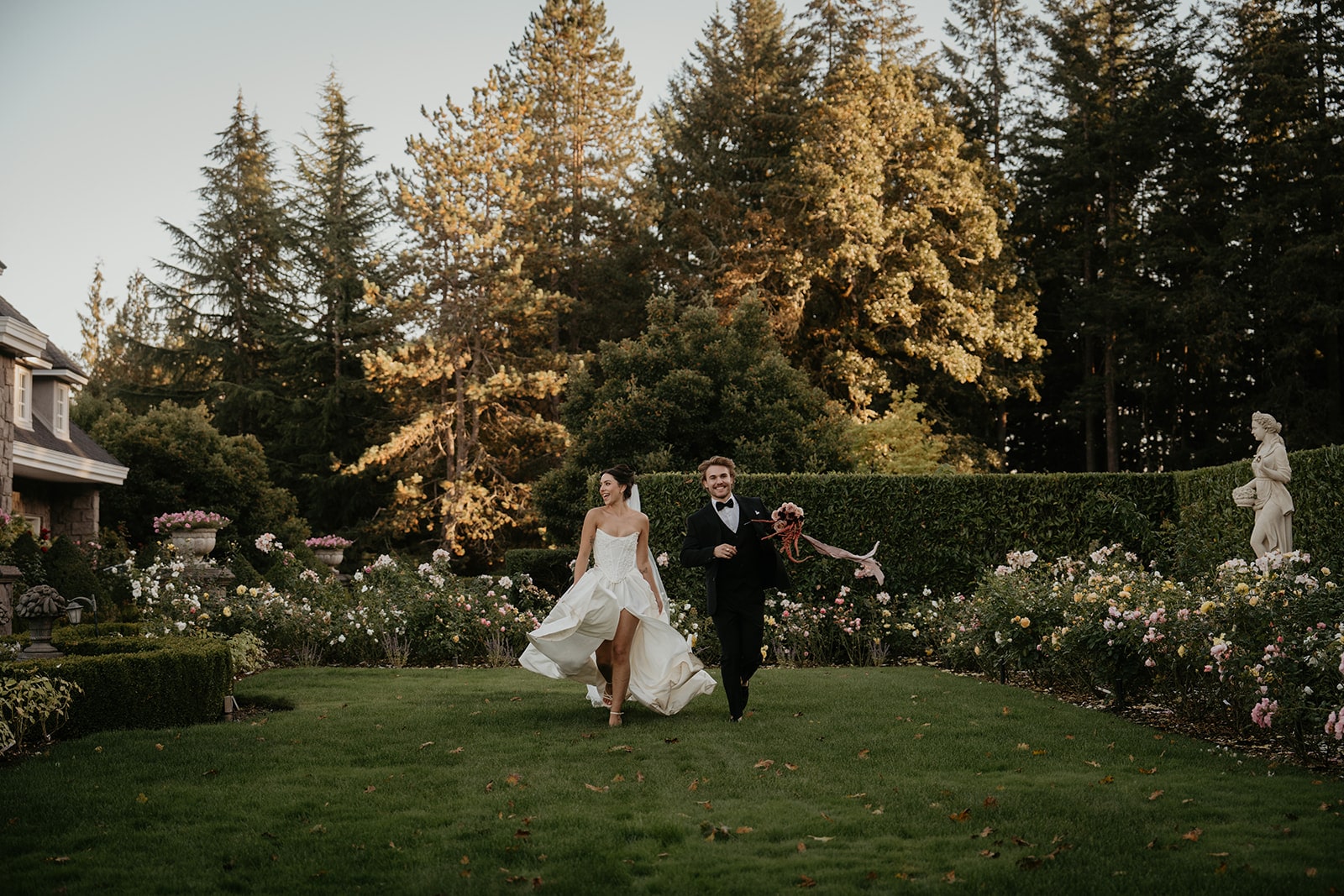 Bride and groom hold hands while running through the gardens at their wedding venue