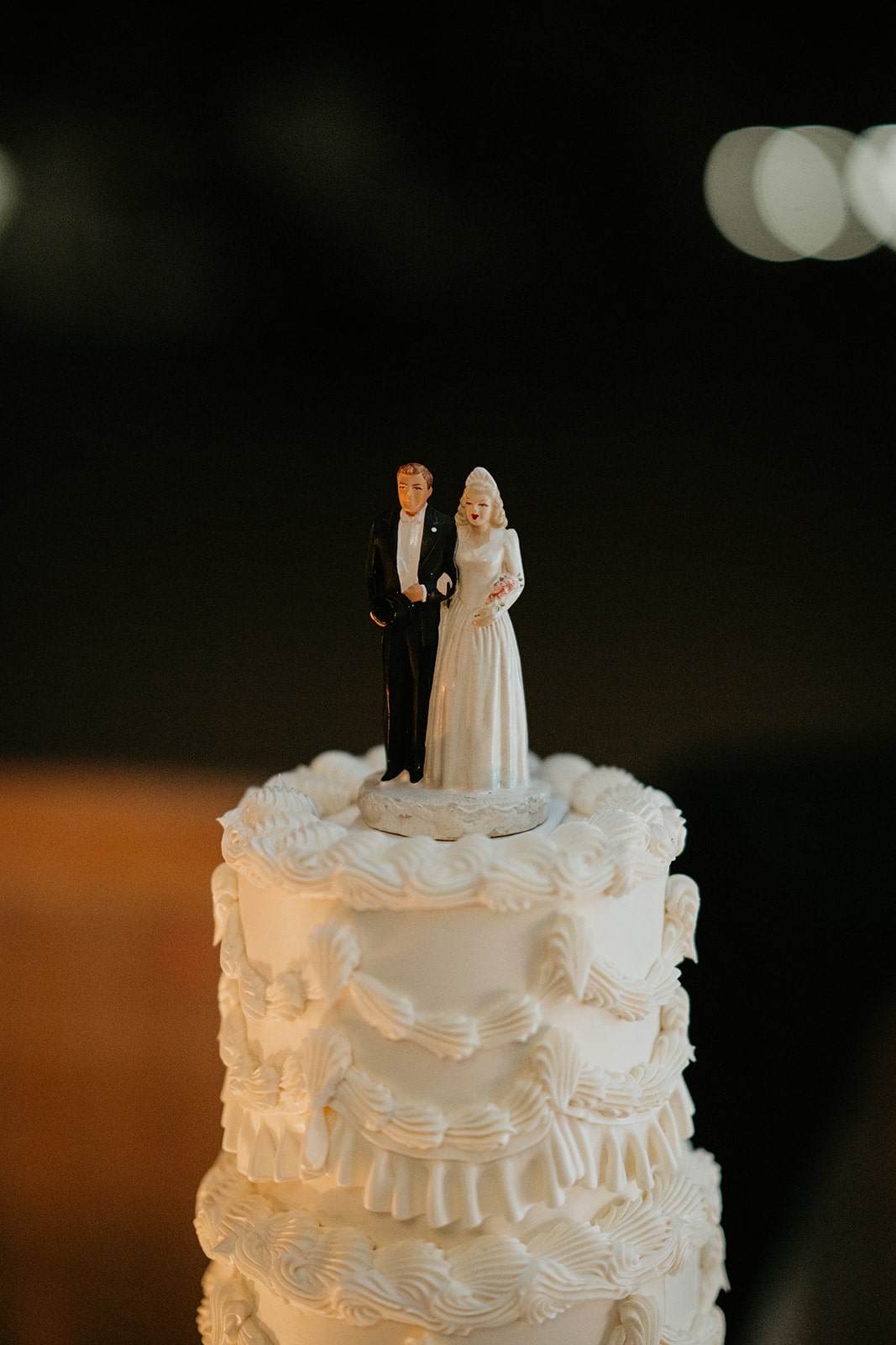 Vintage bride and groom cake topper resting on top of a 3 tier white wedding cake