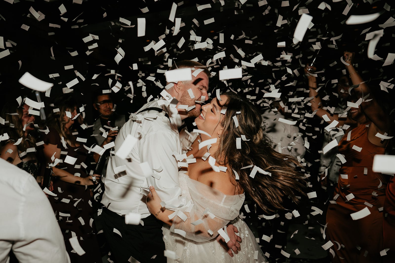 Bride and groom laugh on their wedding reception dance floor while confetti streams all around them. 