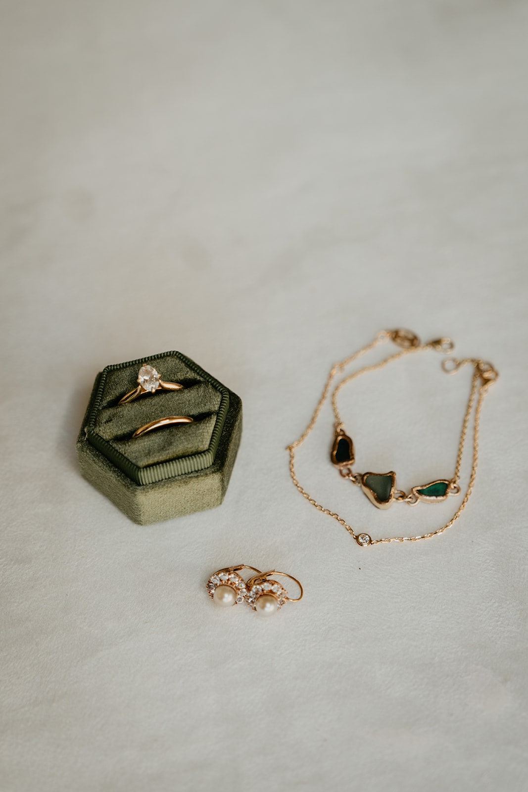 Green velvet ring box with gold wedding bands, gold pearl earrings, and a gold and green stone bracelet