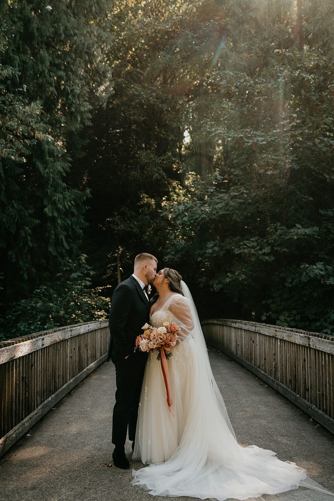 Bride and groom kiss on a bridge in a park during their Ironlight Lake Oswego wedding 