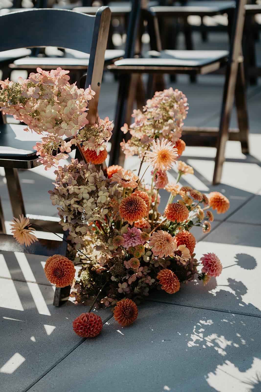 Orange and light pink wedding flower arrangements line wood chairs line an outdoor wedding aisle in Oregon