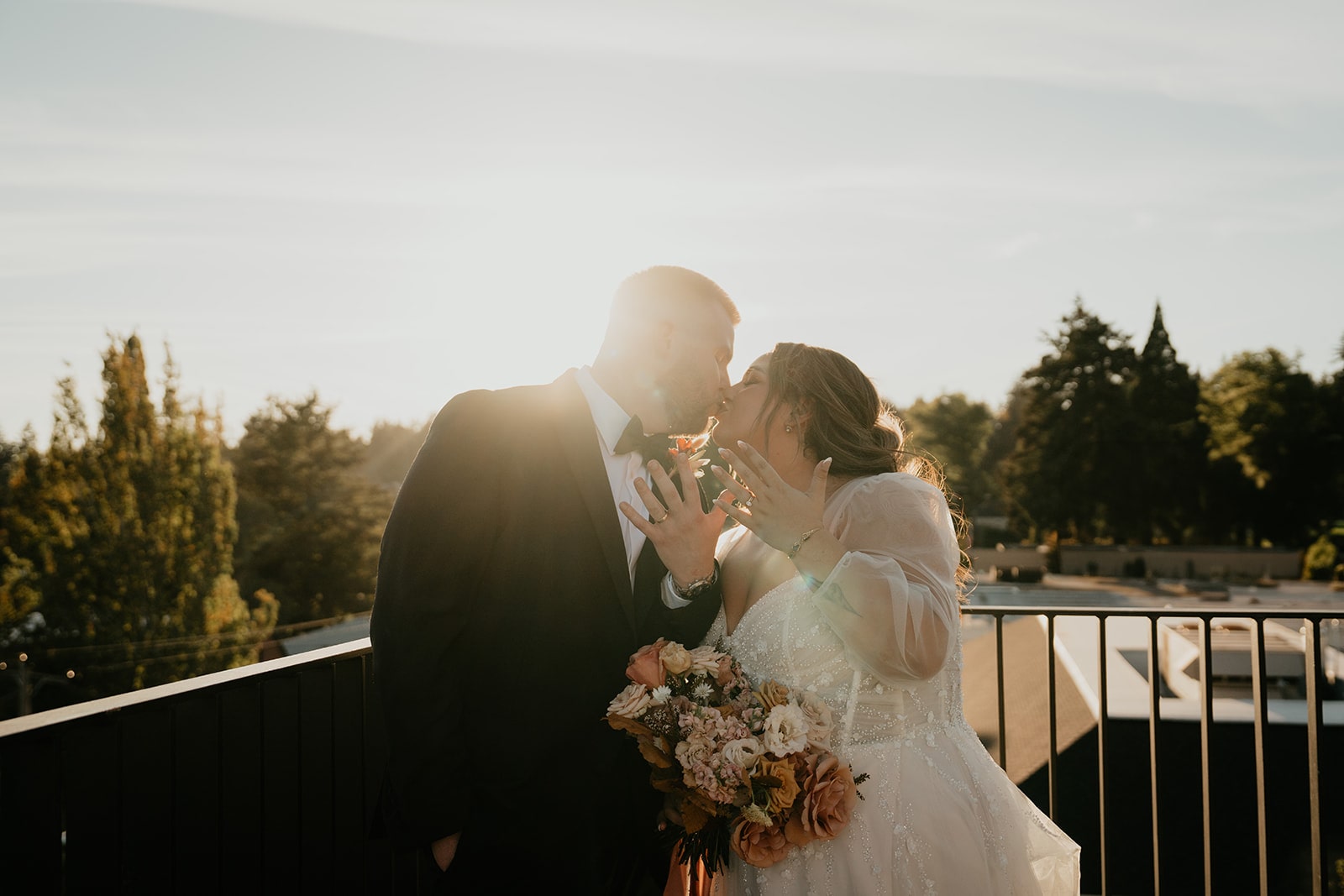 Bride and groom kiss while holding up their ring fingers during their sunset wedding photos at Ironlight