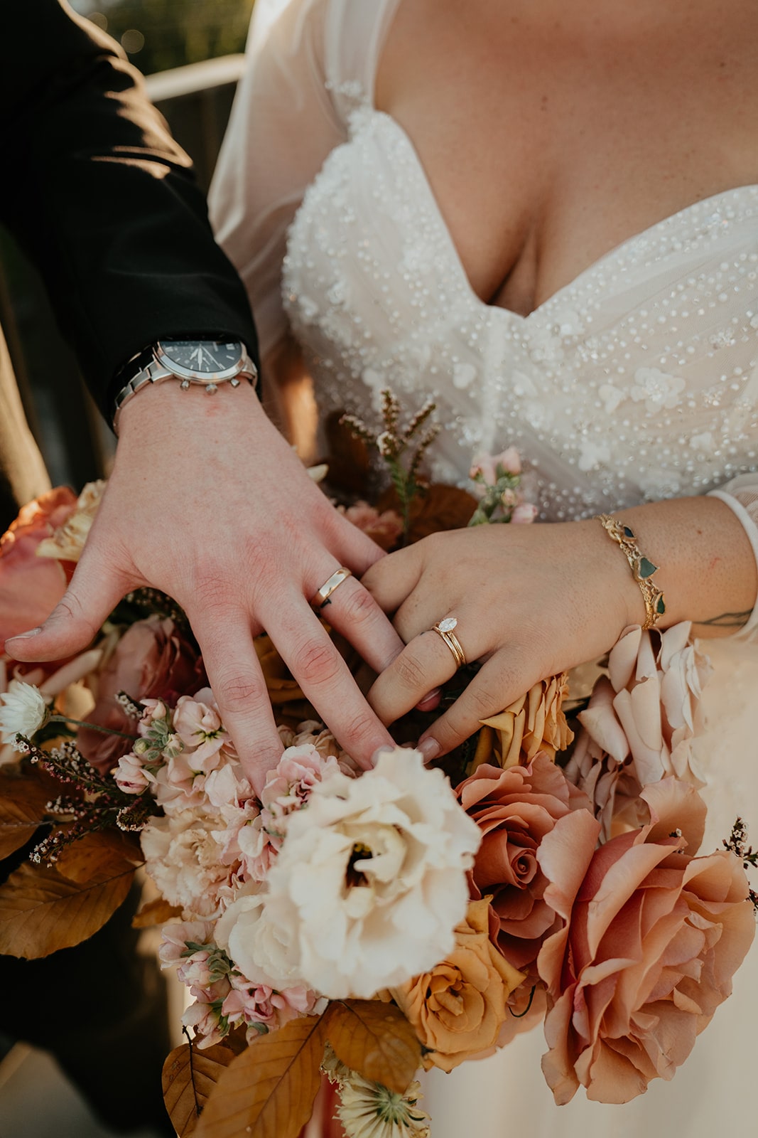 Bride and groom rest their hands on top of their orange and pale pink wedding flowers 