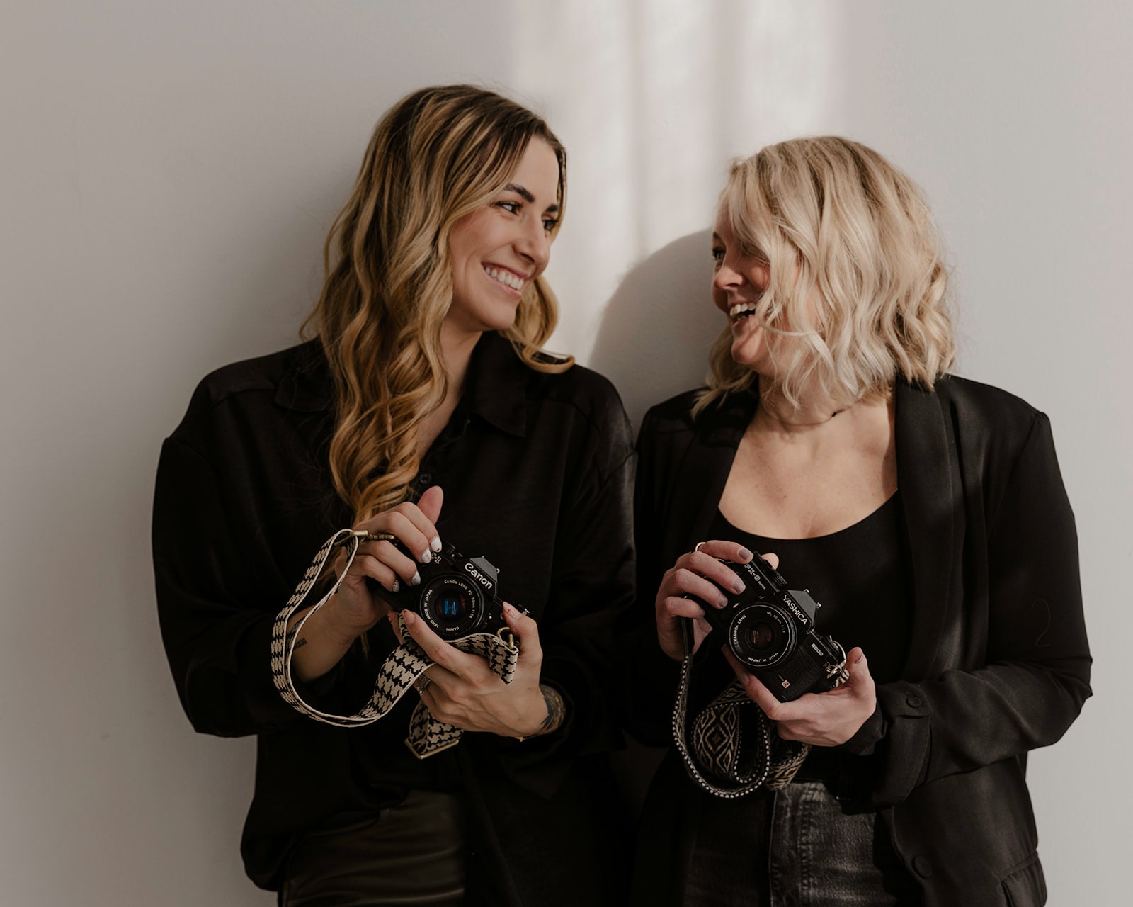 Oregon wedding photographer and associate photographer hold film cameras and smile at each other during their branding session