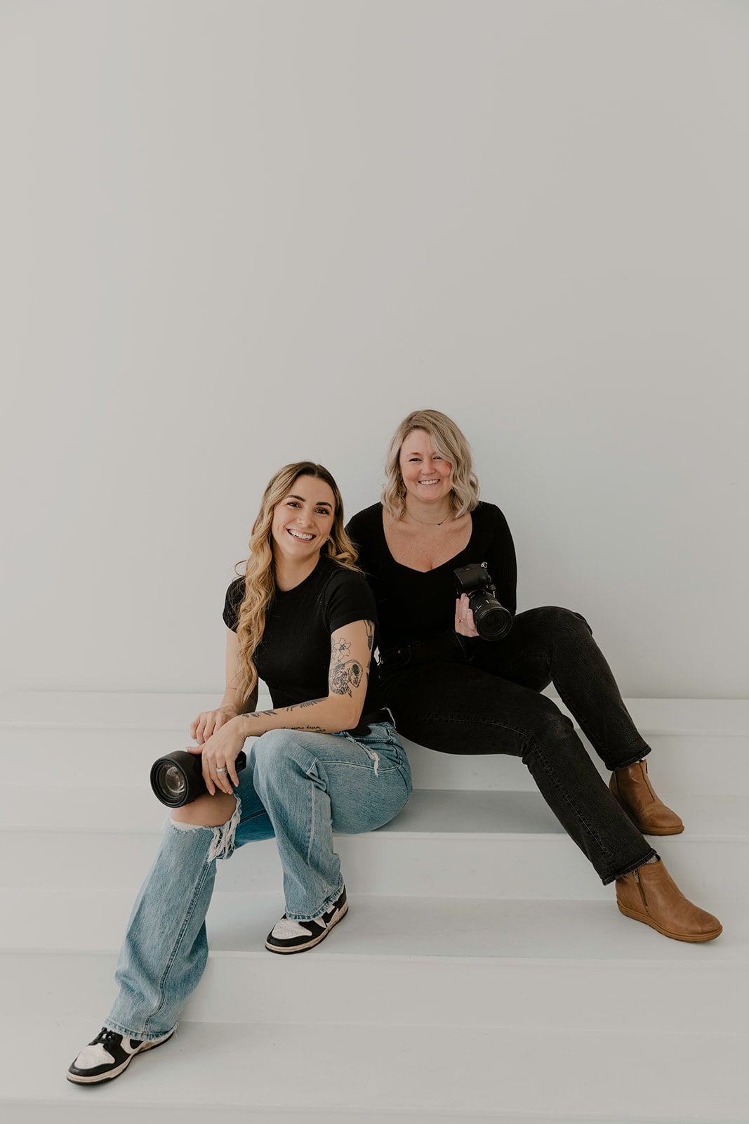 Oregon elopement photographer and associate photographer sit on white steps during their studio branding session