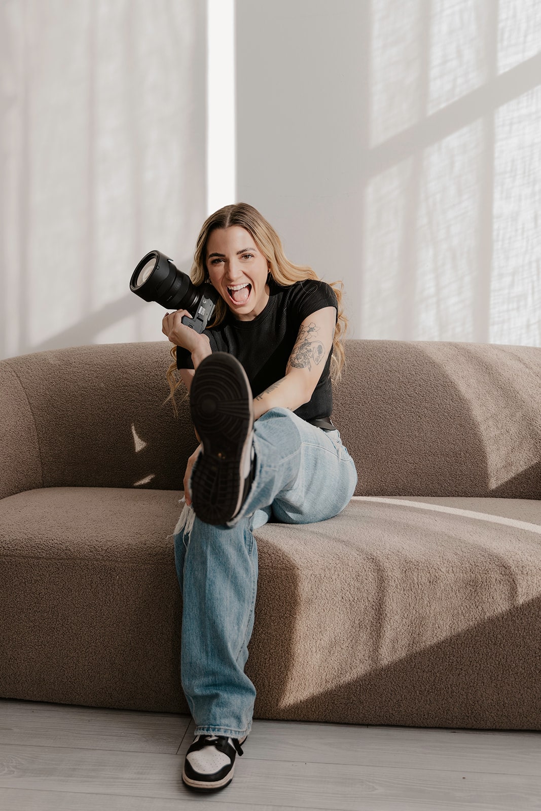 Associate photographer kicks her leg out while sitting on a velvet couch holding a digital camera