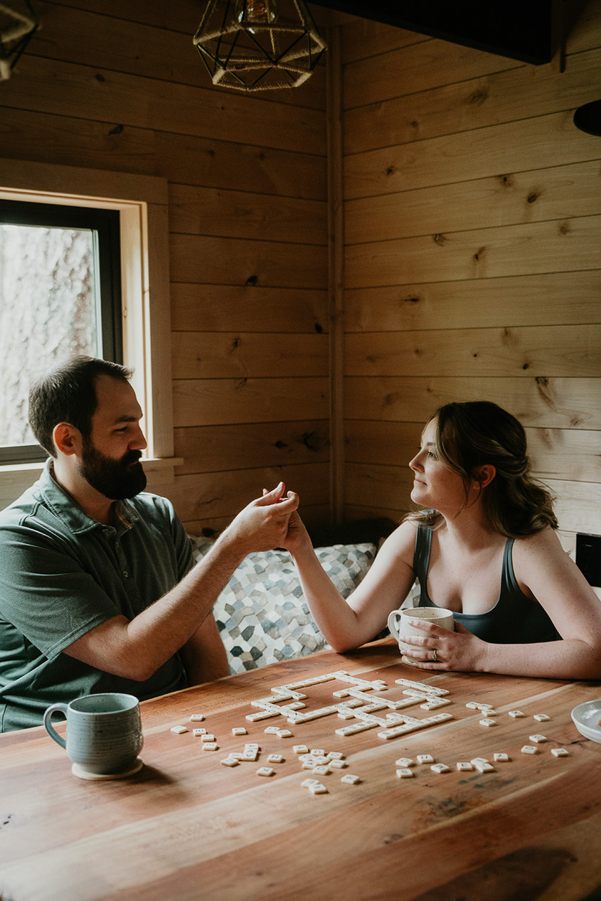 A couple playing Bananagrams in a cozy cabin, a fun an inexpensive activity when considering how much cost it is to elope.