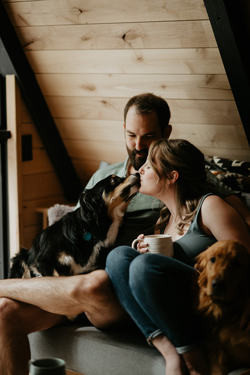 A dog giving her mom kisses while her dad smiles.