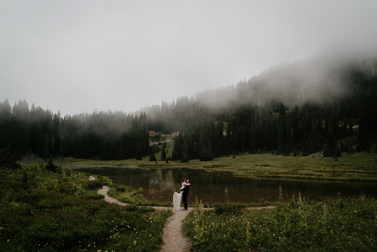 newlyweds kissing by a foggy lake, sweetened by how much more inexpensive the cost for them to elope versus have a traditional wedding is.