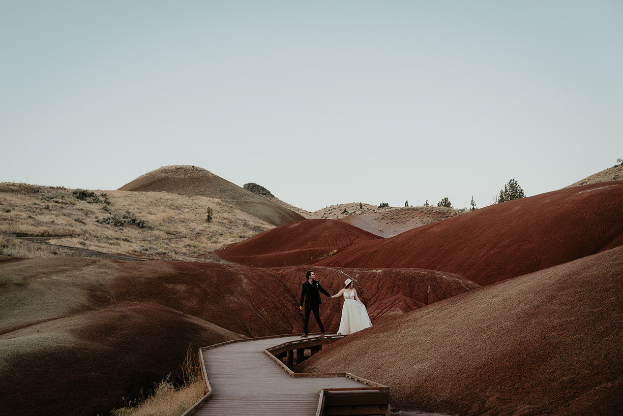 the groom leading his bride through the painted hills in Oregon during their elopement.