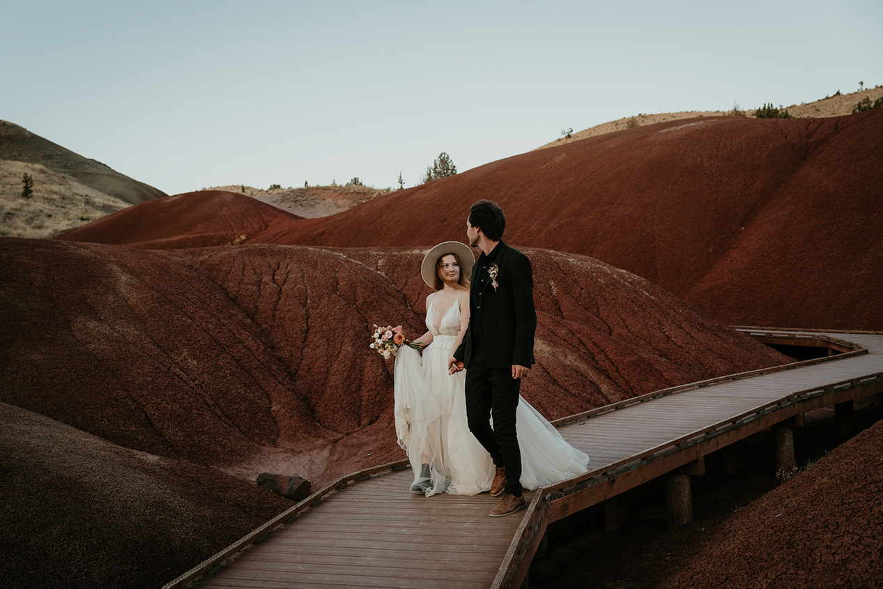 the newlyweds hiking on a wooden boardwalk through red hills.