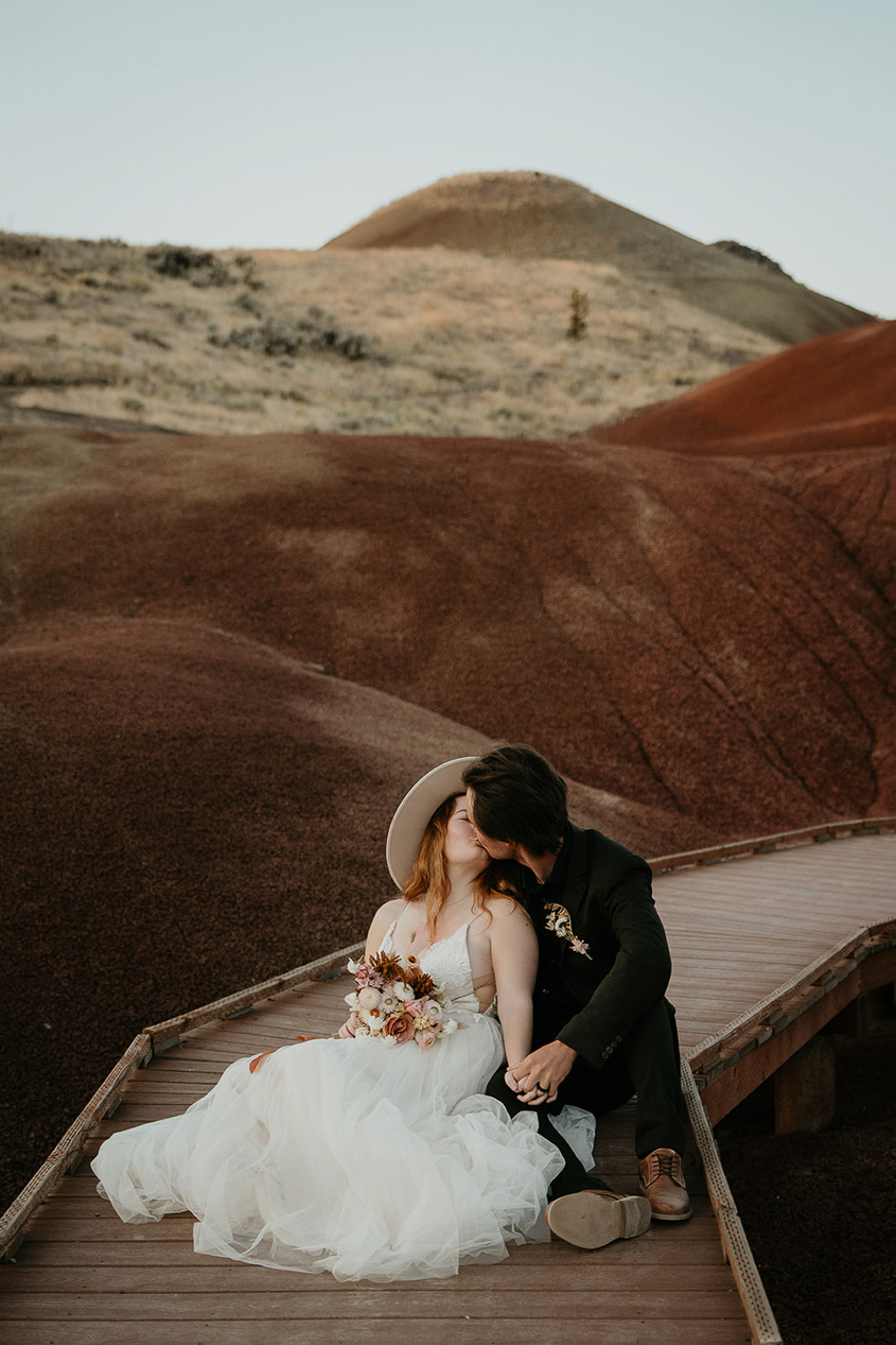 newlyweds kissing while sitting on a boardwalk during their painted hills elopement.