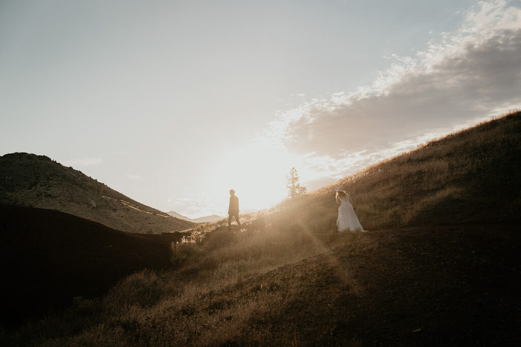 the newlyweds hiking on a trail in their wedding clothes at sunset.