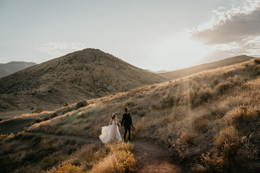 the newlyweds hiking on a trail with the sun setting in the background.