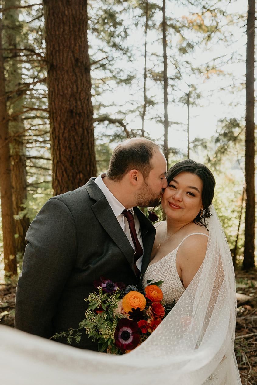 the husband kissing his bride in the forest.