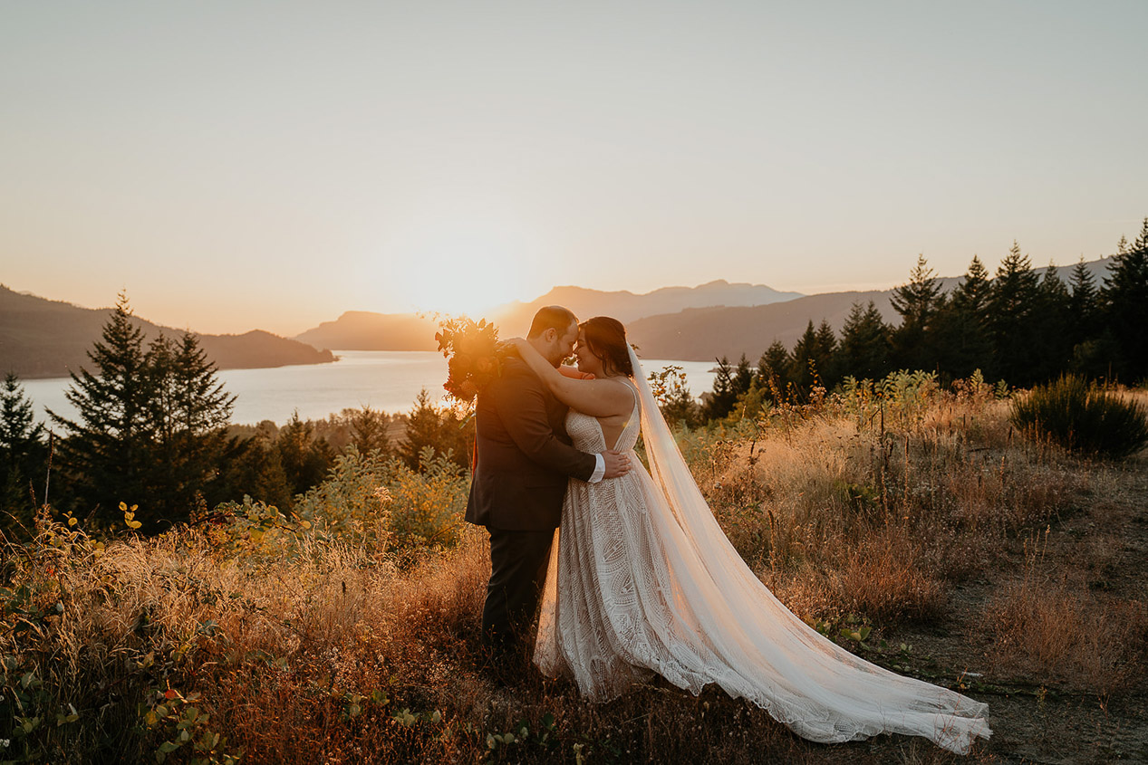 the newlyweds hugging while standing by a lake at sunset during their wind mountain ranch wedding.