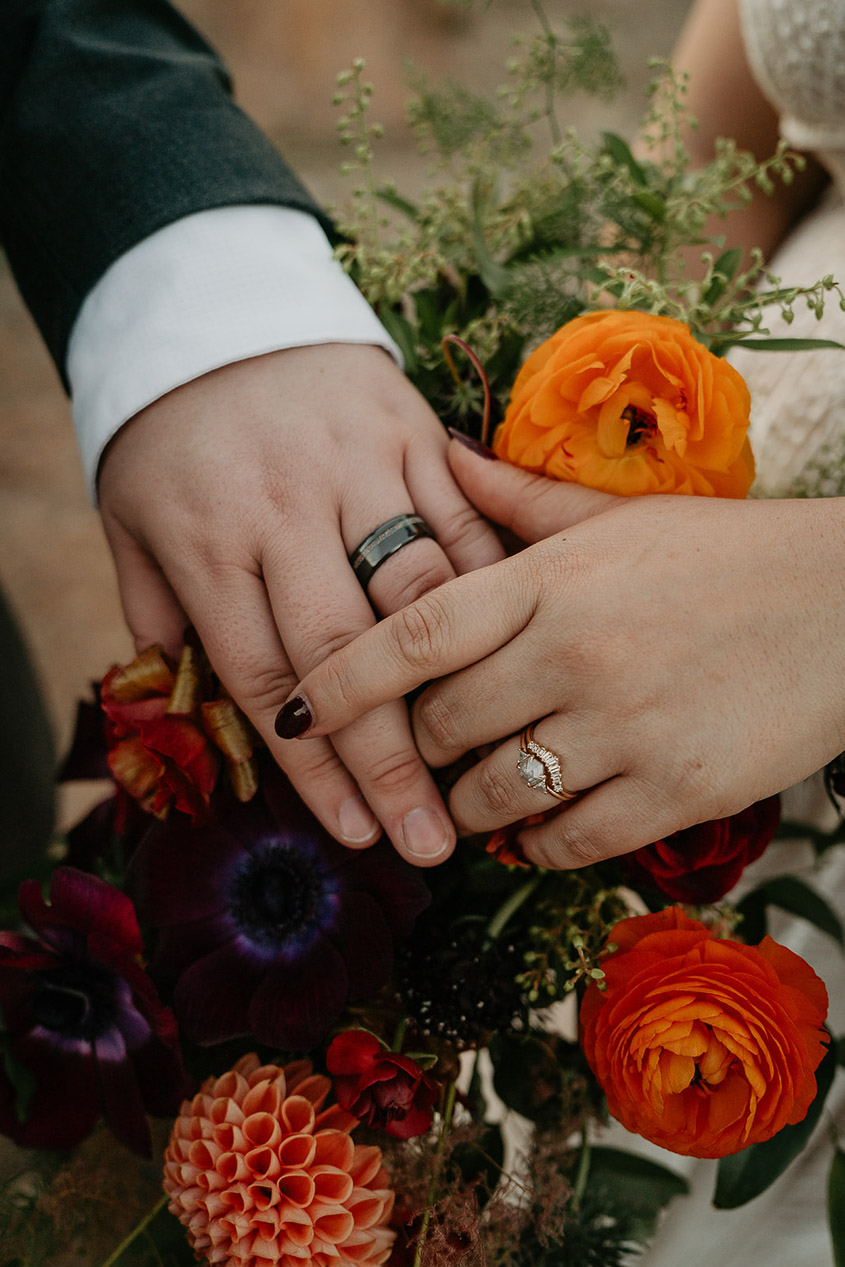 the bride and groom's hands on top of a bouquet of flowers.