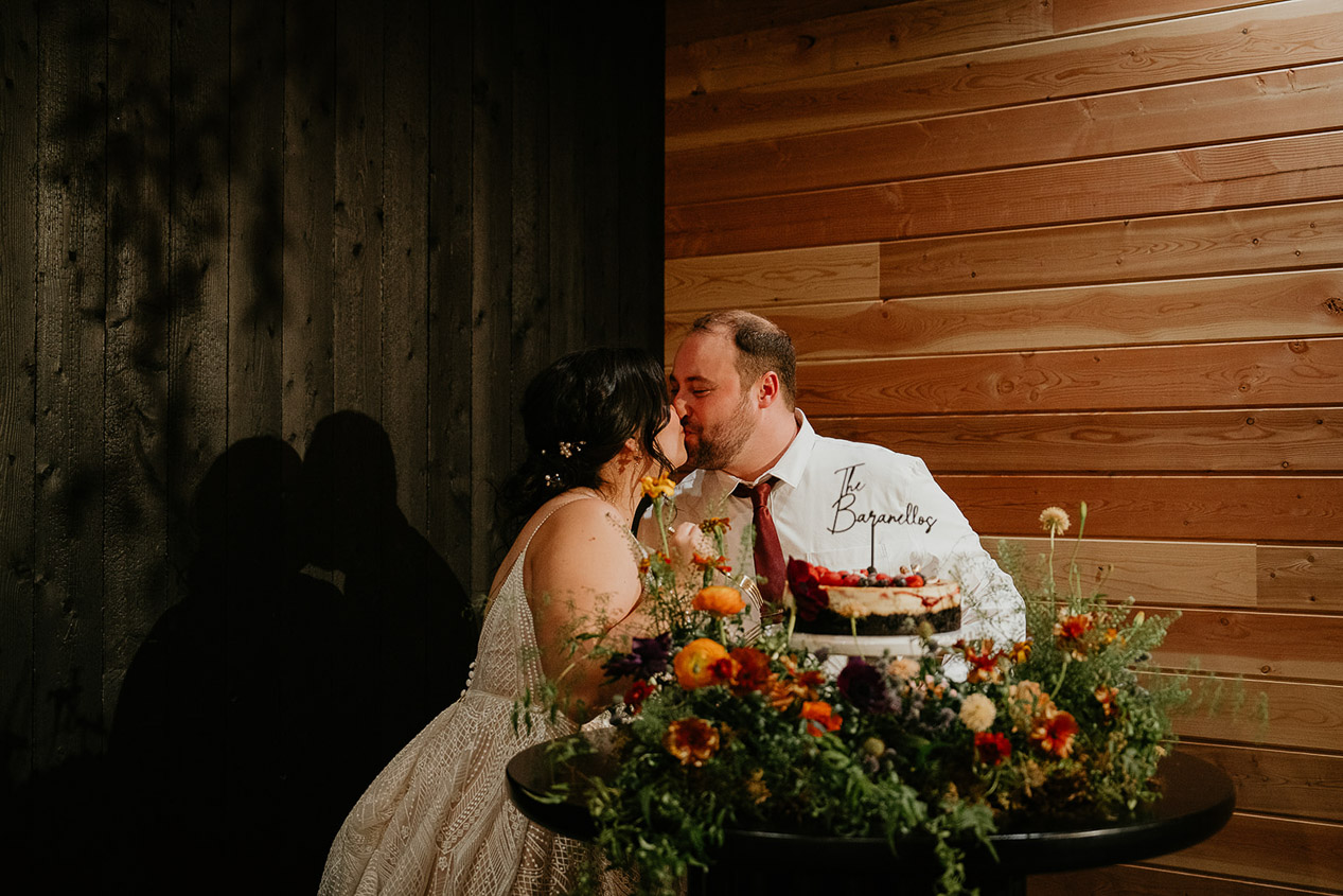 the newlyweds kissing by their wedding cake during their wind mountain ranch wedding.