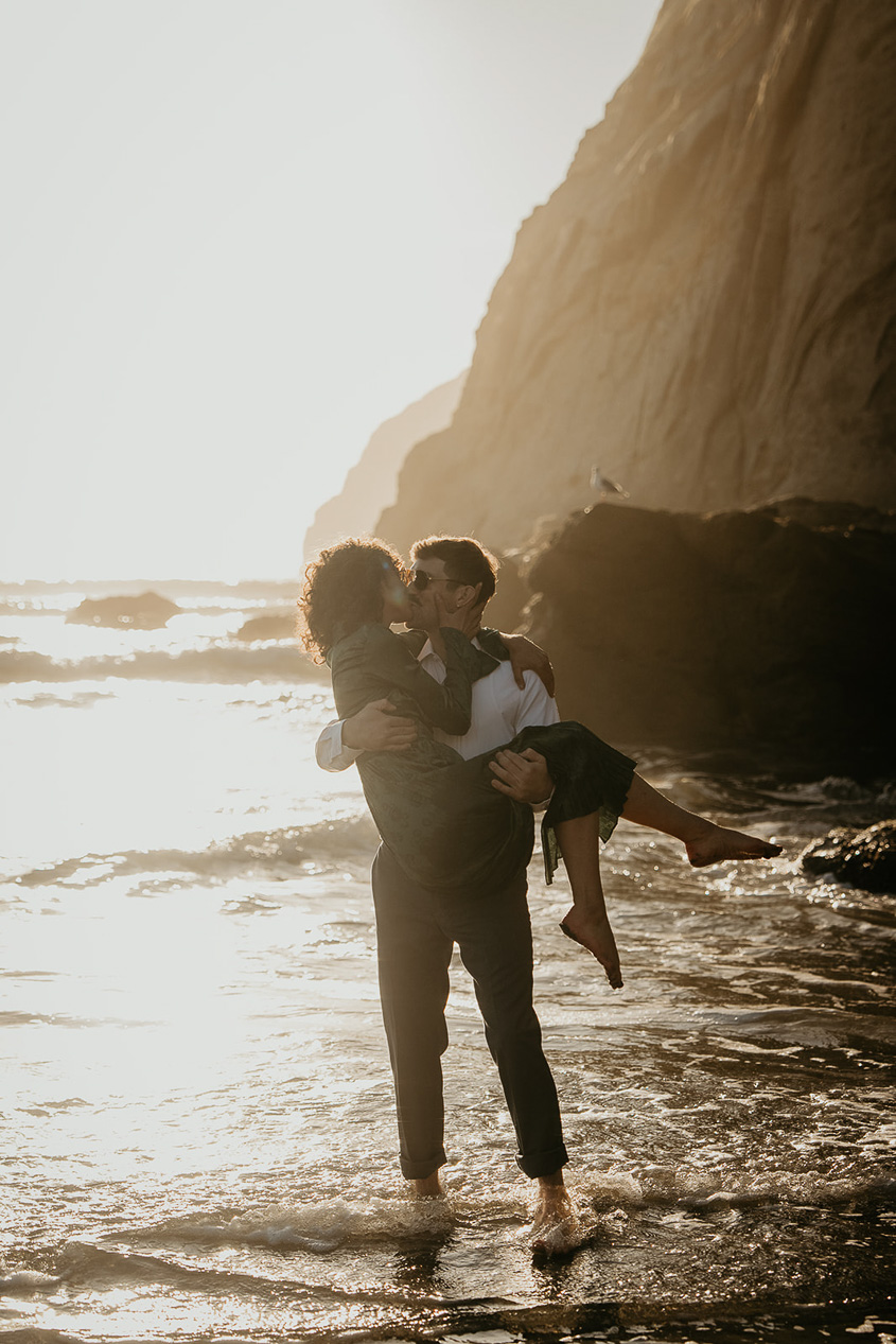 a couple dancing in the ocean during their cape kiwanda engagement.