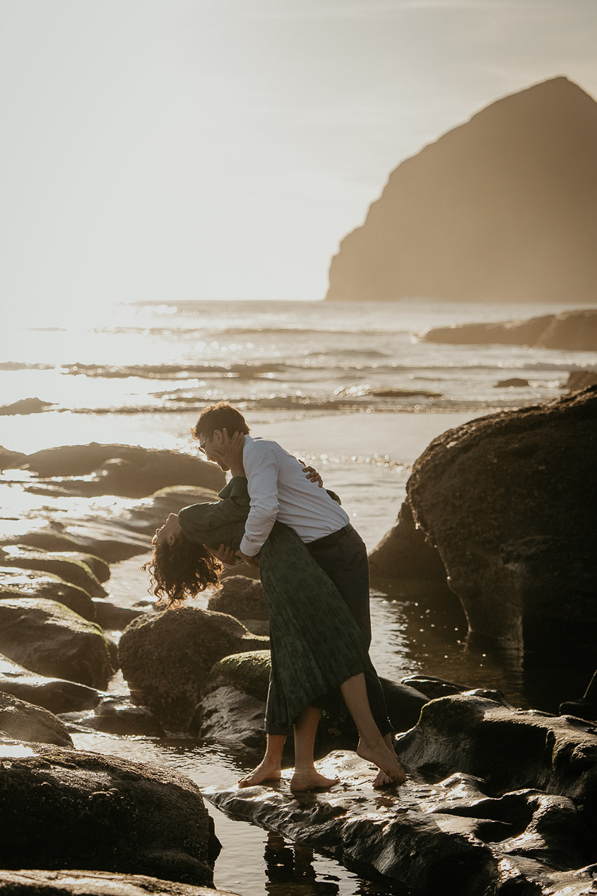 a couple dancing on the rocks by the ocean during their cape kiwanda engagement.