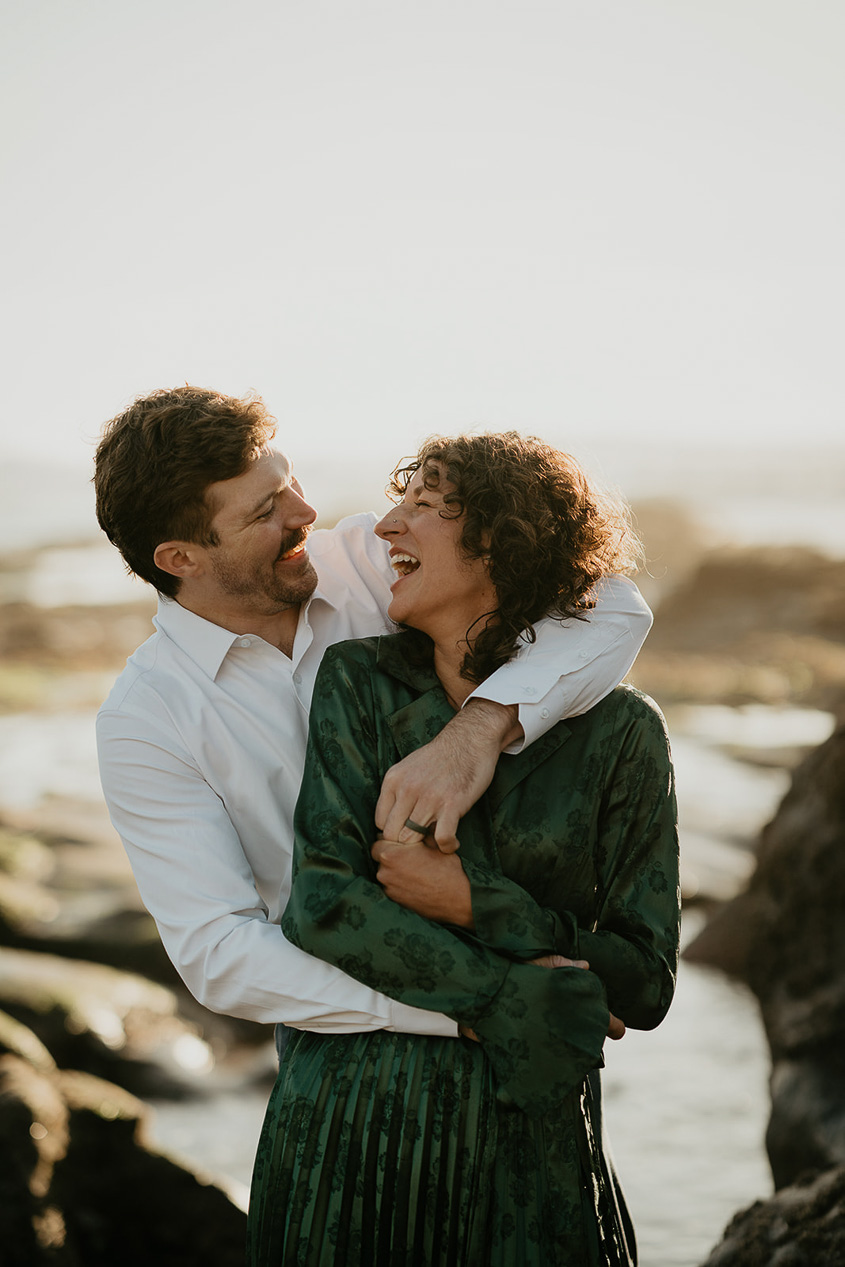 A couple hugging each other and smiling along the Oregon coastline.