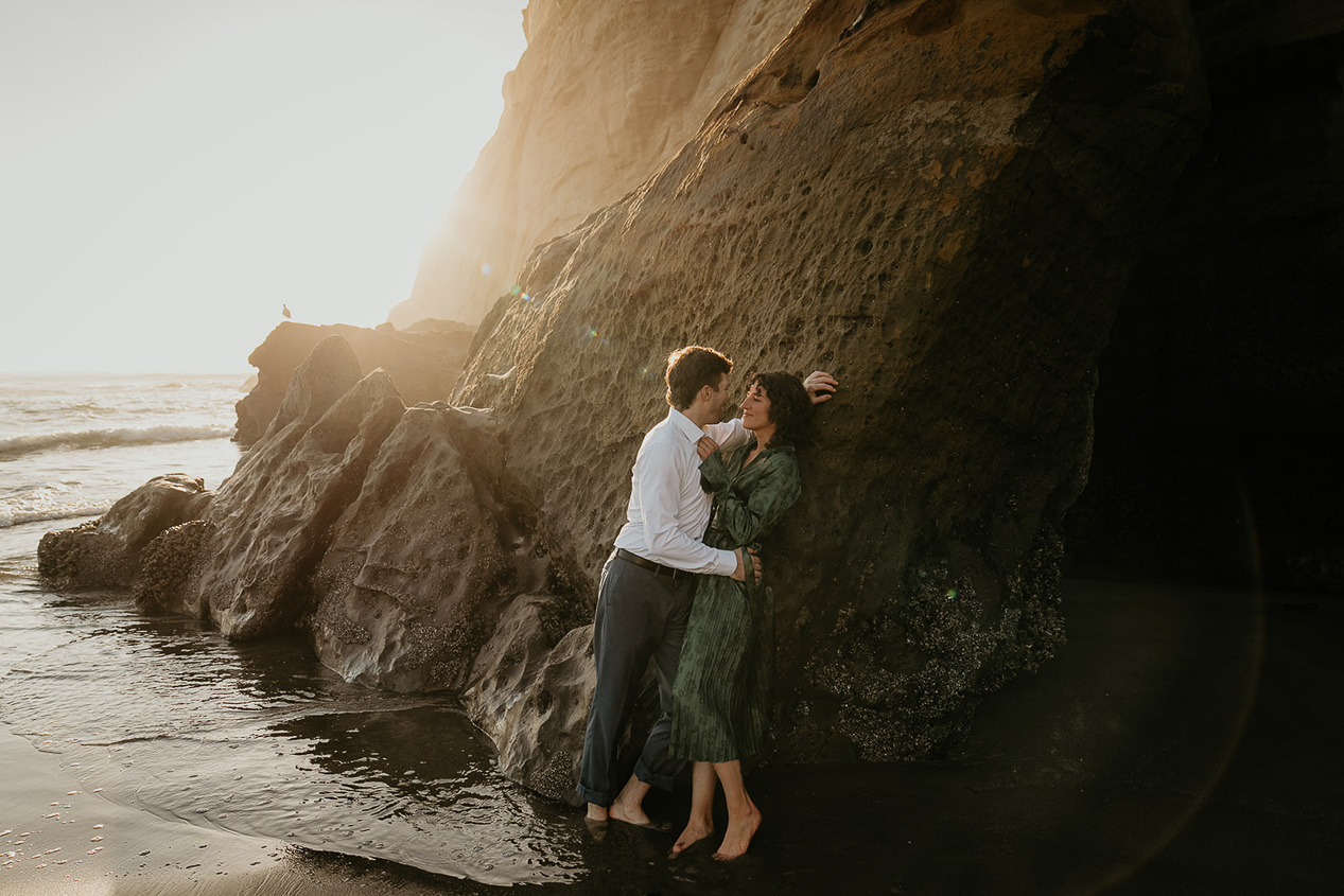 A couple holding each other against a cliffside during their cape kiwanda engagement.