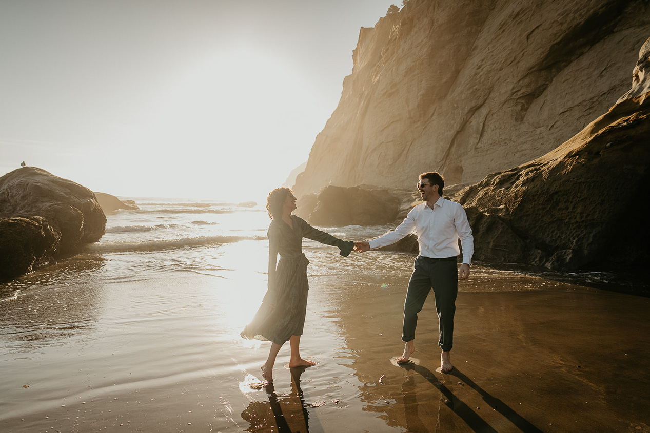 a couple holding hands and dancing as the sun sets on their cape kiwanda engagement.