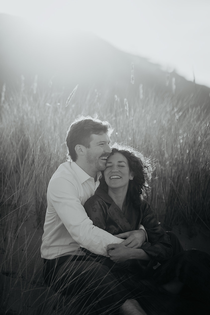 a couple smiling and holding each other in a grassy field.