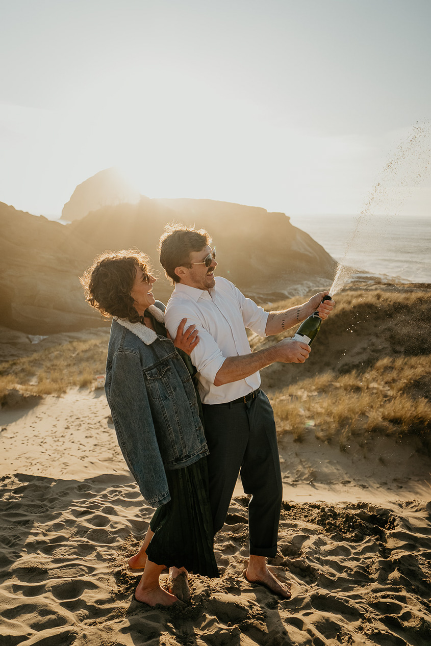 a couple popping a bottle of champagne during their cape kiwanda engagement