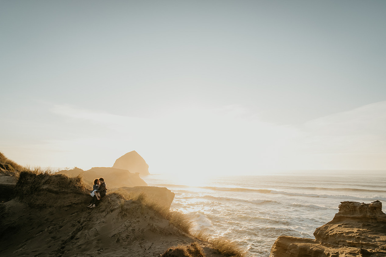 a couple holding each other on a sandy dune during their Cape Kiwanda Engagement.