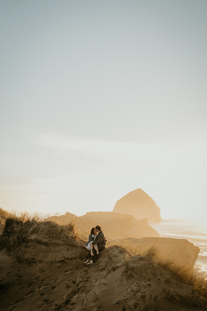 a couple kissing on a sand dune at sunset during their Cape Kiwanda Engagement.