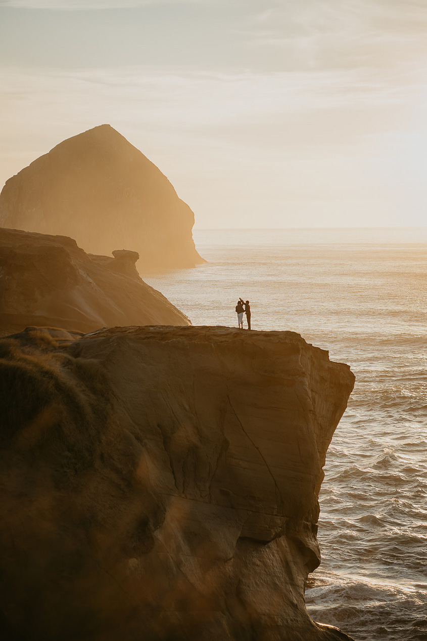 a couple dancing on an ocean cliff with the coastline and a sea stack in the background during their Cape Kiwanda Engagement.