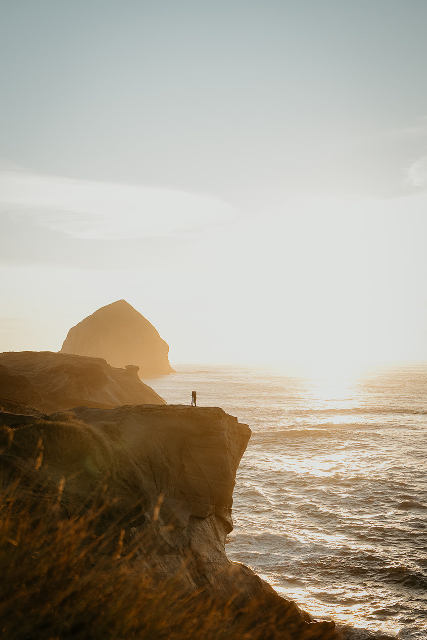 a couple dancing on a cliff at sunset, with the Oregon coastline and a sea stack in the background during their Cape Kiwanda Engagement.