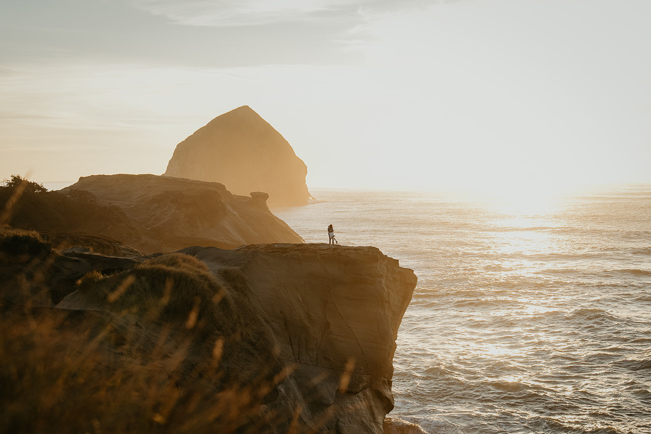 a couple dancing on a cliff with the Oregon coastline and a sea stack in the background during their Cape Kiwanda Engagement.